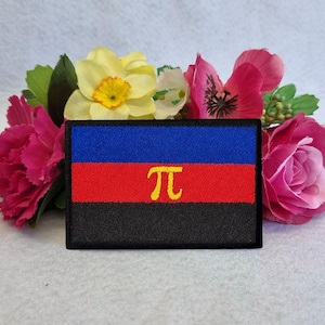 Pode incluir: Um remendo bordado preto, vermelho, azul e amarelo com o símbolo "π" no centro.