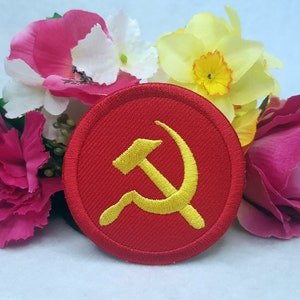 May include: A red circular patch with a yellow embroidered hammer and sickle.