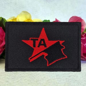 May include: A black fabric patch with a red star and the letters "TA" inside. The star is superimposed over a black silhouette of a hammer and sickle.