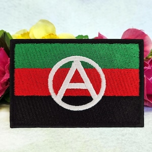 May include: A black, red and green embroidered patch with a white circle containing a white letter "A" with a circle around it.