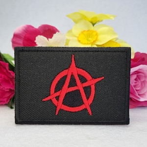 Puede incluir: Parche bordado negro con un símbolo de anarquía rojo. El símbolo es un círculo con una A en su interior y una línea diagonal que lo atraviesa.