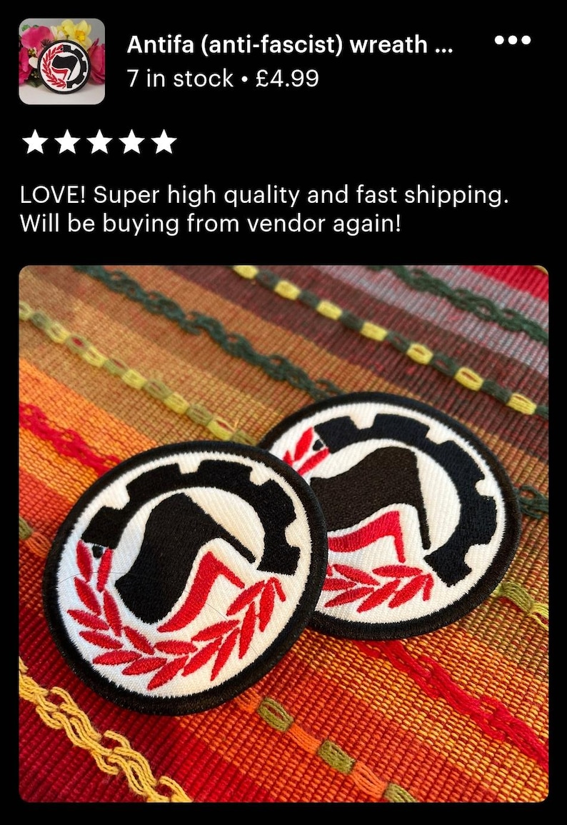 May include: Two black and red embroidered patches with a stylized black boot, a red heel, and a black flag with a red stripe on a white background. The patches are surrounded by a red wreath and a black gear. The patches are on a red, orange, and yellow woven fabric.