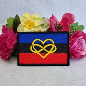 May include: A black, blue, and red embroidered patch with a yellow infinity symbol in the shape of a heart. The patch is surrounded by pink flowers.
