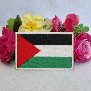 May include: An embroidered Palestinian flag patch with a red triangle, black, white, and green stripes. The patch is surrounded by pink and yellow flowers.