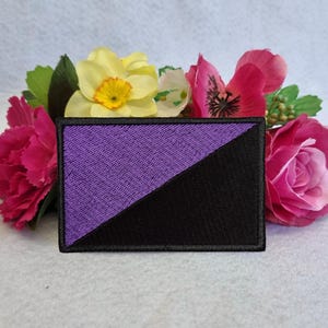 May include: Purple and black embroidered patch with a diagonal line dividing the colors. The patch is surrounded by a white border.