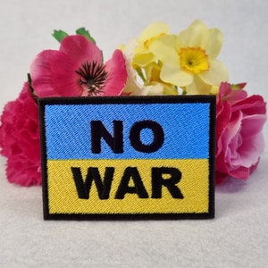May include: A blue and yellow embroidered patch with the text "NO WAR" in black. The patch is surrounded by pink and yellow flowers.