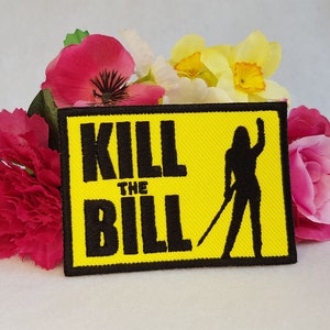 May include: Yellow embroidered patch with black text that reads "KILL THE BILL" and a black silhouette of a woman holding a sword.