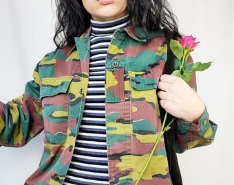 May include: A green, brown, and yellow camouflage jacket with a black and white striped turtleneck shirt and a black and red plaid skirt.
