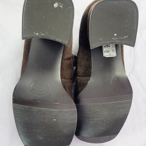 May include: A pair of brown suede heeled shoes with black soles. The shoes have a lace-up design and a small tag on the right shoe that says "8 1/2".