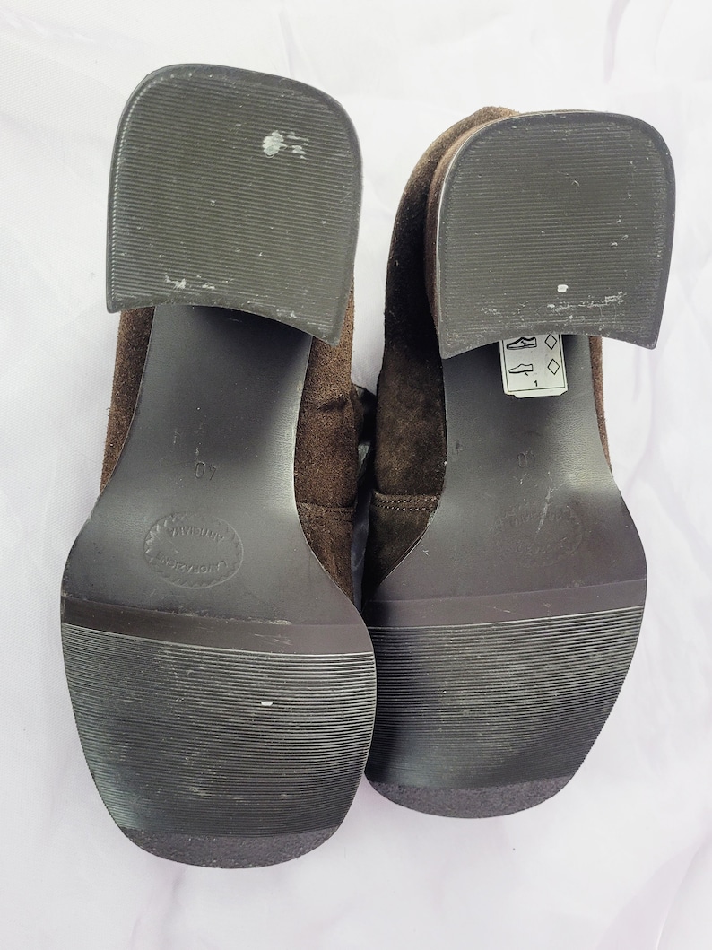 May include: A pair of brown suede heeled shoes with black soles. The shoes have a lace-up design and a small tag on the right shoe that says "8 1/2".