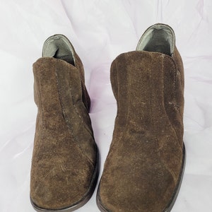 May include: A pair of brown suede ankle boots with a rounded toe and a low heel.
