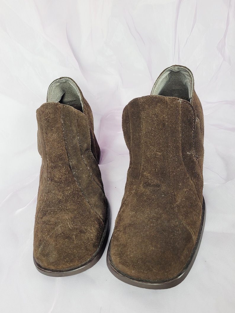 May include: A pair of brown suede ankle boots with a rounded toe and a low heel.