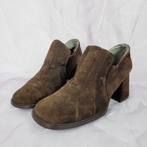 May include: A pair of brown suede ankle boots with a block heel. The boots have a simple design and are made of soft suede.