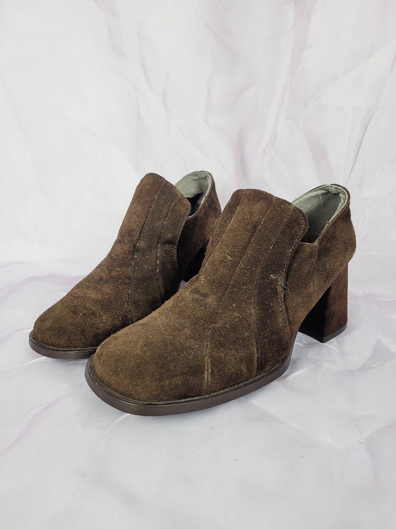 May include: A pair of brown suede ankle boots with a block heel. The boots have a simple design and are made of soft suede.