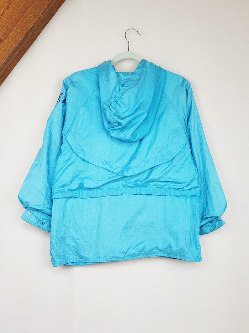 May include: A bright turquoise hooded jacket hangs on a light green hanger. The jacket has a drawstring waist and elastic cuffs. The material has a slight sheen. The jacket is a vintage style.