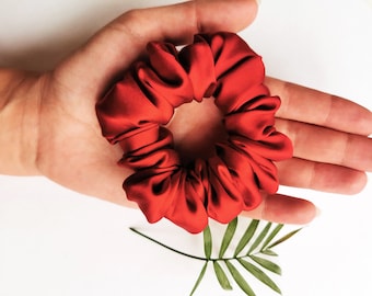May include: A red satin scrunchie for hair. The scrunchie is made of soft, silky fabric and is designed to be gentle on hair.