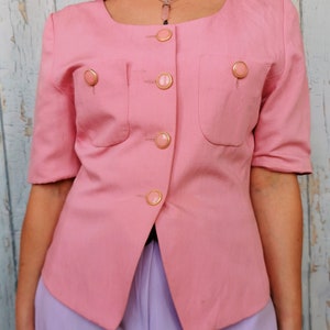 May include: A pink blazer with gold buttons and a scoop neck. The blazer has two pockets on the front and is made of a lightweight fabric.