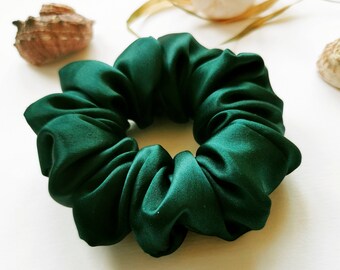 May include: A dark green satin scrunchie hair tie. The scrunchie is made of soft, silky fabric and is designed to be gentle on hair.