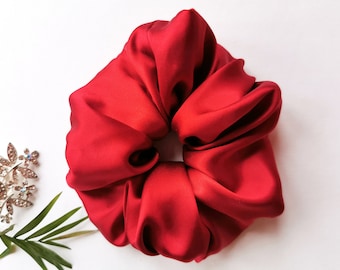 May include: A bright red satin scrunchie for hair. The scrunchie is made of soft, smooth fabric and is designed to be gentle on hair.