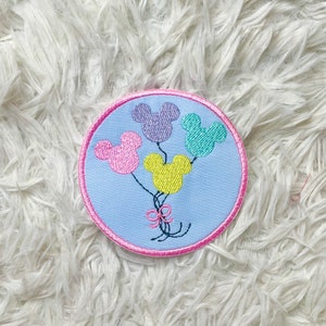 Könnte beinhalten: Ein blauer und rosa gestickter Aufnäher mit vier Mickey-Maus-förmigen Ballons in Rosa, Lila, Grün und Gelb.