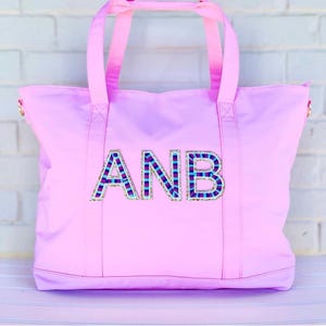 May include: A pink canvas tote bag with the name "ANB" in colourful, glittery letters.