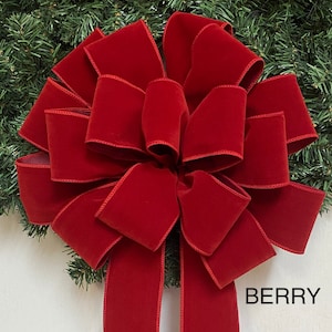May include: A large, berry-colored velvet bow with long tails, set against a backdrop of green pine needles. The bow is richly textured and features stitched edges. The word "BERRY" is printed at the bottom of the image. Ideal for holiday decor.