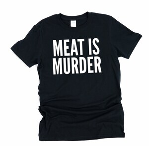 Puede incluir: Camiseta negra con el texto blanco "MEAT IS MURDER". La camiseta de cuello redondo est&aacute; hecha de un material suave. El texto est&aacute; centrado en la parte delantera de la camiseta.