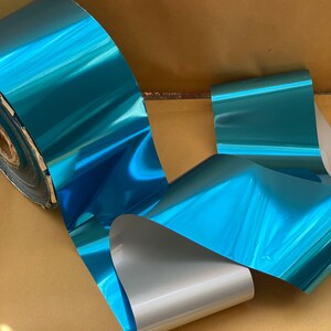 Op de afbeelding: Een rol teal metallic folie met een zilveren achterkant. De folie is glanzend en reflecterend.