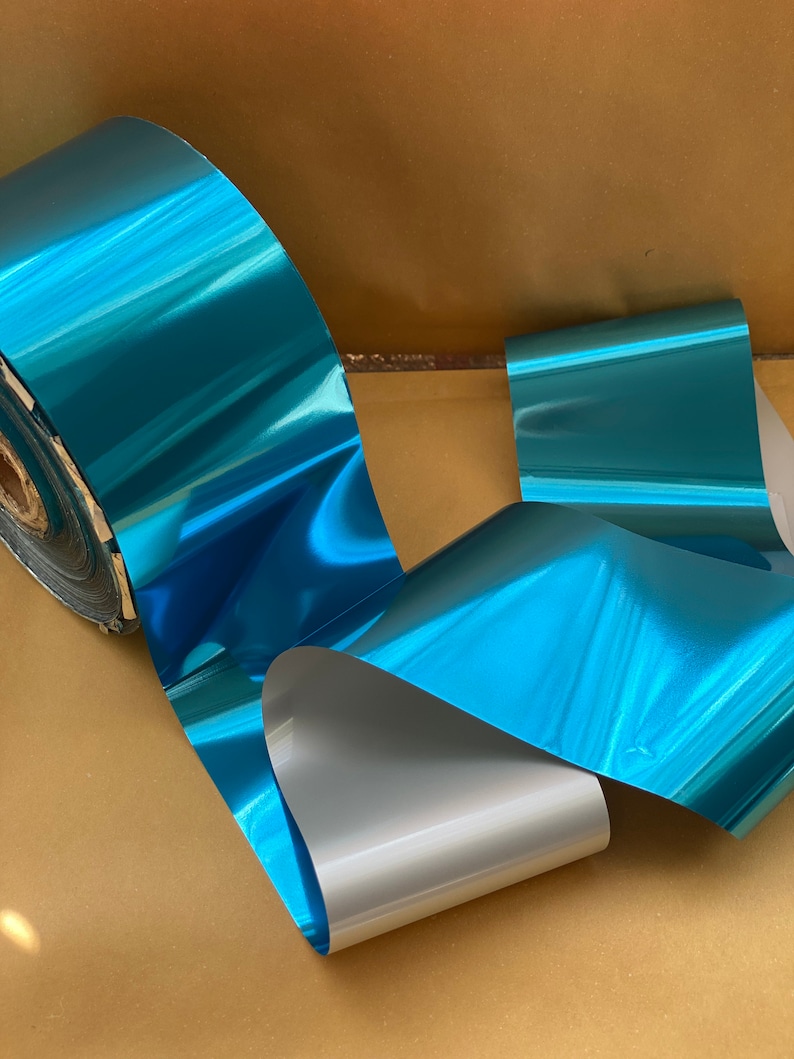 Op de afbeelding: Een rol teal metallic folie met een zilveren achterkant. De folie is glanzend en reflecterend.