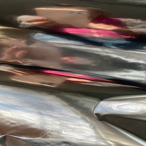 Op de afbeelding: Close-up van een zwarte, glanzende en gekreukelde stof met een lichte roze reflectie.