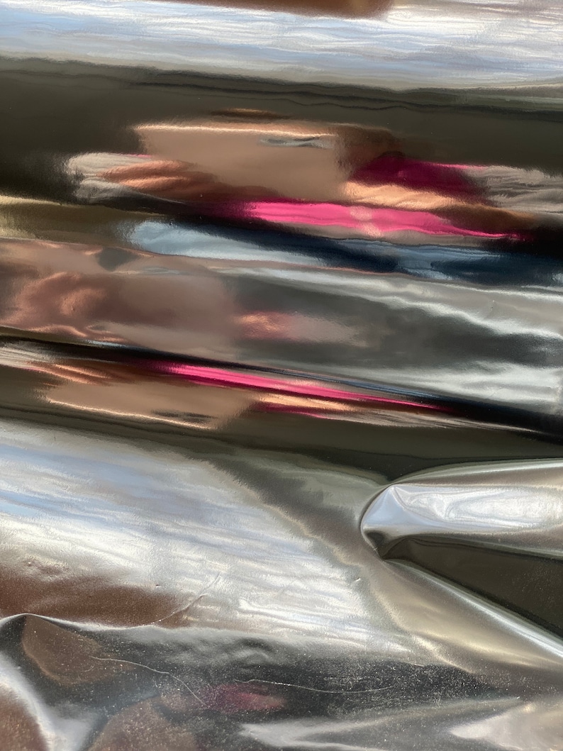 Op de afbeelding: Close-up van een zwarte, glanzende en gekreukelde stof met een lichte roze reflectie.