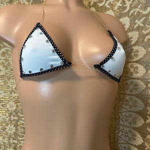 May include: White bikini top with black trim and clear straps. The top is decorated with small rhinestones.