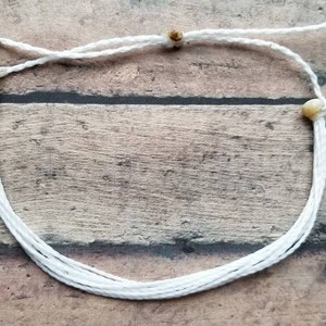 May include: White string bracelet with wooden beads. The bracelet is made of multiple strands of string and has a simple design.