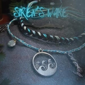 May include: A collection of ocean-themed jewelry, including a blue and white braided bracelet, a pendant with wave designs, and a mermaid charm. The text "Siren's Wake" is written in a teal font.