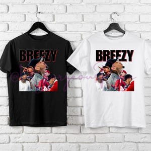 May include: Two t-shirts with a black and white image of a group of people with the word "Breezy" printed in red and black letters.