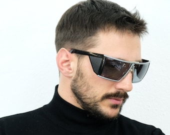 May include: A man wearing a black turtleneck sweater and blue jeans. He is wearing silver-rimmed sunglasses with dark lenses.