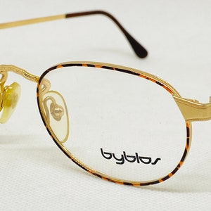 May include: Gold-rimmed eyeglasses with a tortoiseshell frame and the word "Byblos" printed on the lens.