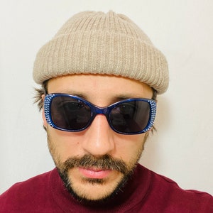 Puede incluir: Una persona con una boina beige y gafas de sol azules con pedrer&iacute;a. Lleva un jersey de cuello alto color granate.