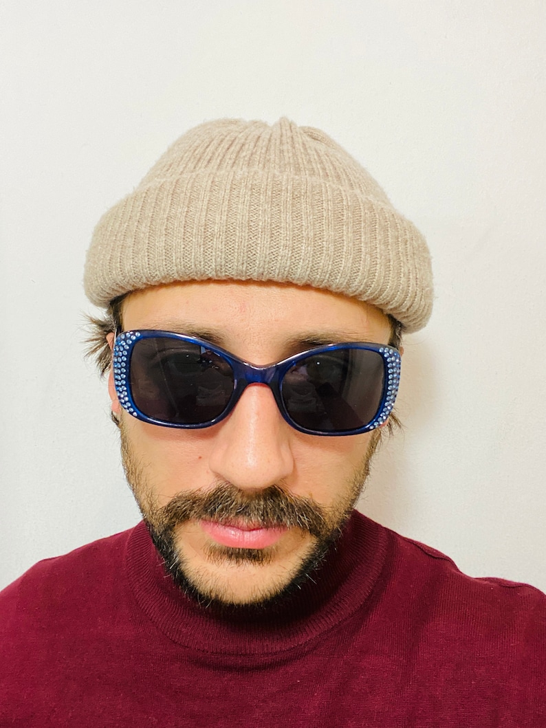 Puede incluir: Una persona con una boina beige y gafas de sol azules con pedrer&iacute;a. Lleva un jersey de cuello alto color granate.