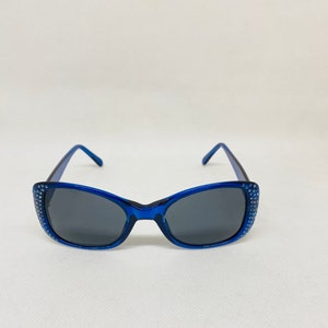 Puede incluir: Gafas de sol azules con pedrer&iacute;a alrededor del marco y lentes oscuras.