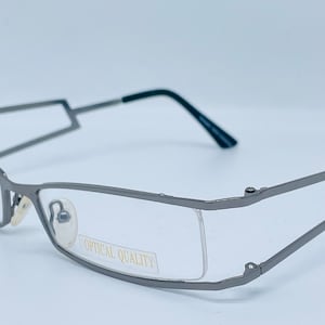 May include: A pair of silver-toned metal eyeglasses with a rectangular frame and clear lenses. The lenses have the words "OPTICAL QUALITY" printed on them.