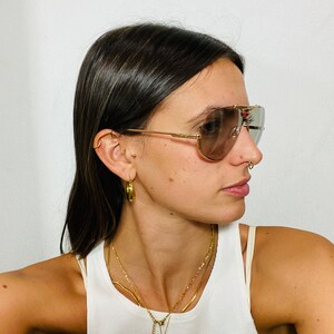 May include: A woman wearing gold hoop earrings, a gold chain necklace with a small octopus pendant, and a pair of brown aviator sunglasses with gold frames.