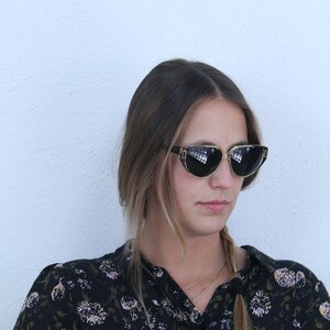 以下が含まれることがあります： 黒色のサングラスと黒色の花柄のブラウスを着た、長い茶色の髪の女性