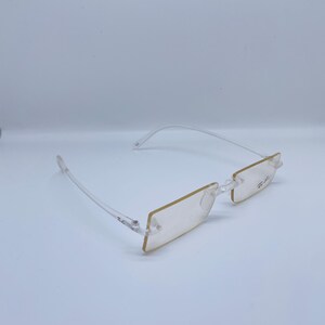 May include: Clear plastic frame glasses with a rectangular lens shape. The glasses have a subtle gold tint.