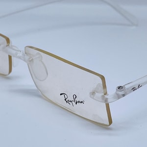 May include: Clear plastic frame eyeglasses with a rectangular lens shape. The Ray-Ban logo is printed on the right lens.