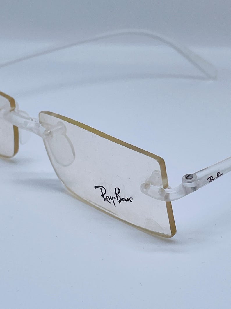 May include: Clear plastic frame eyeglasses with a rectangular lens shape. The Ray-Ban logo is printed on the right lens.
