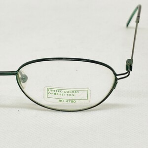 Puede incluir: Gafas negras y verdes con montura verde y lentes ovaladas. Las gafas tienen una etiqueta que dice "UNITED COLORS OF BENETTON." y "8C 4790."