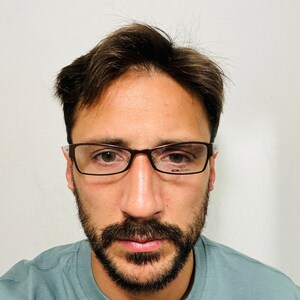 May include: Rectangular eyeglasses with a brown frame and clear lenses. The glasses have a thin frame and are worn by a person with a beard and short brown hair. The person is wearing a light blue t-shirt.