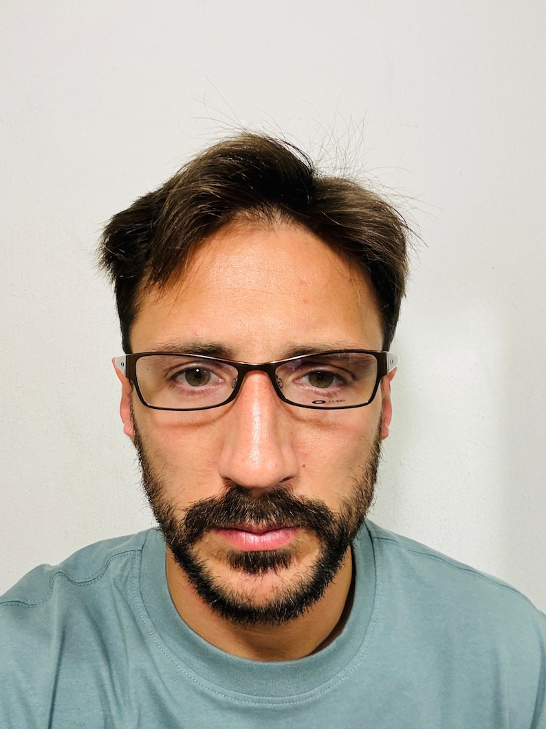 May include: Rectangular eyeglasses with a brown frame and clear lenses. The glasses have a thin frame and are worn by a person with a beard and short brown hair. The person is wearing a light blue t-shirt.