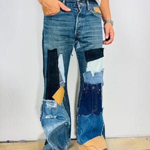 Può includere: Jeans di denim blu con più toppe di denim e tessuto di diversi colori. I jeans sono svasati in fondo.